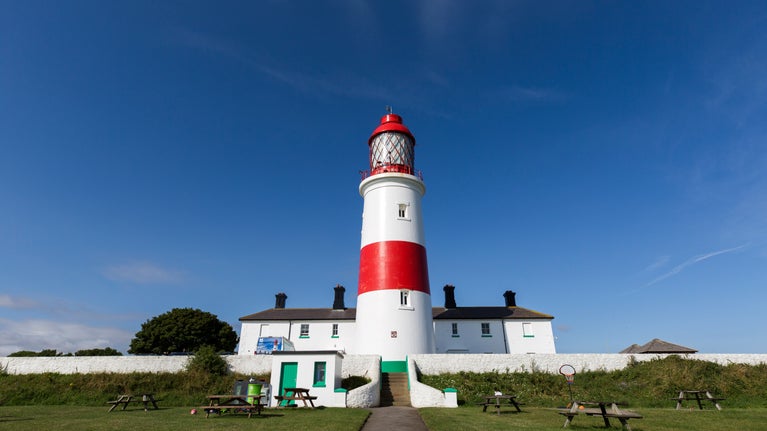 The red and white striped tower of Souter Lighthouse and surrounding white buildings in sunshine against a clear blue sky